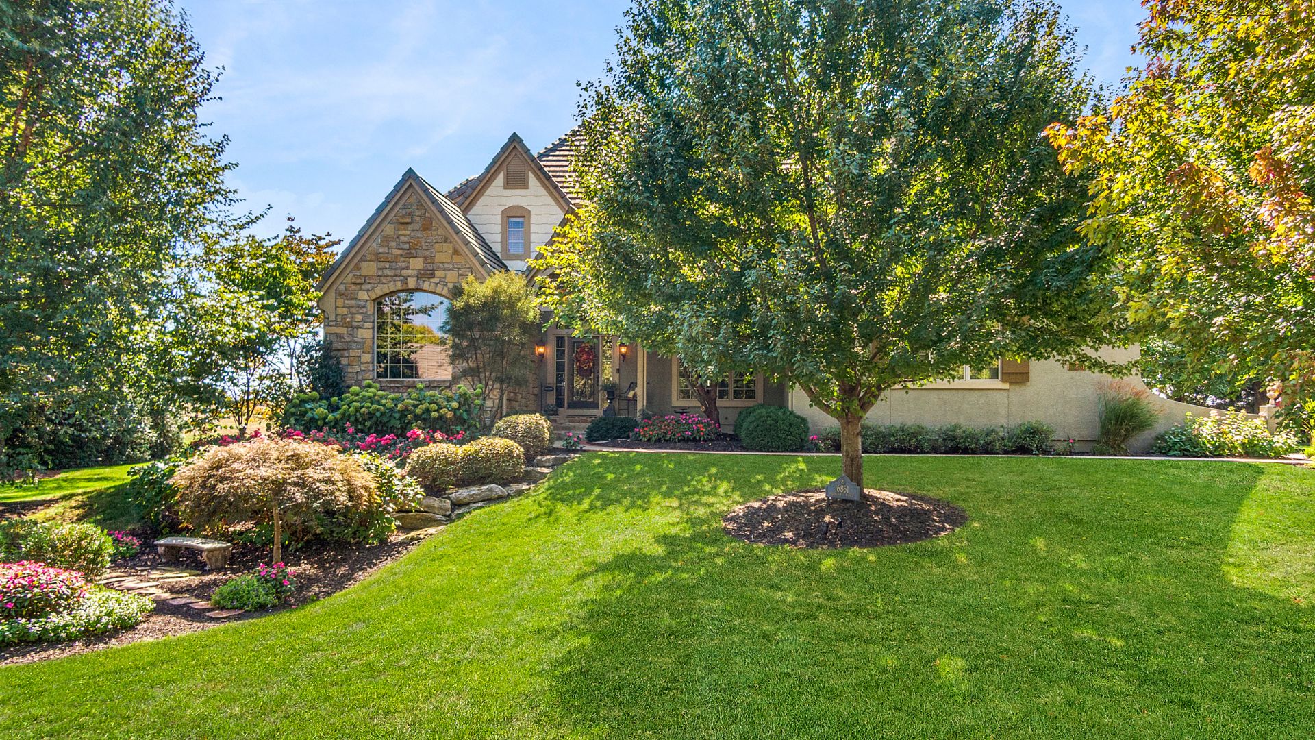Front photo of a home with stone and a tree in front covering half of the home. Beautiful landscaping.
