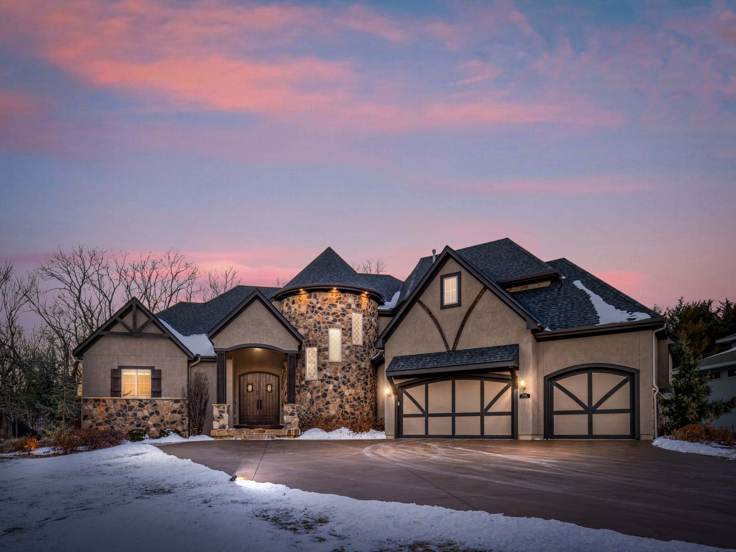 Front twilight photo of a large castle-like home with a three car garage taken in the winter with snow on the ground.