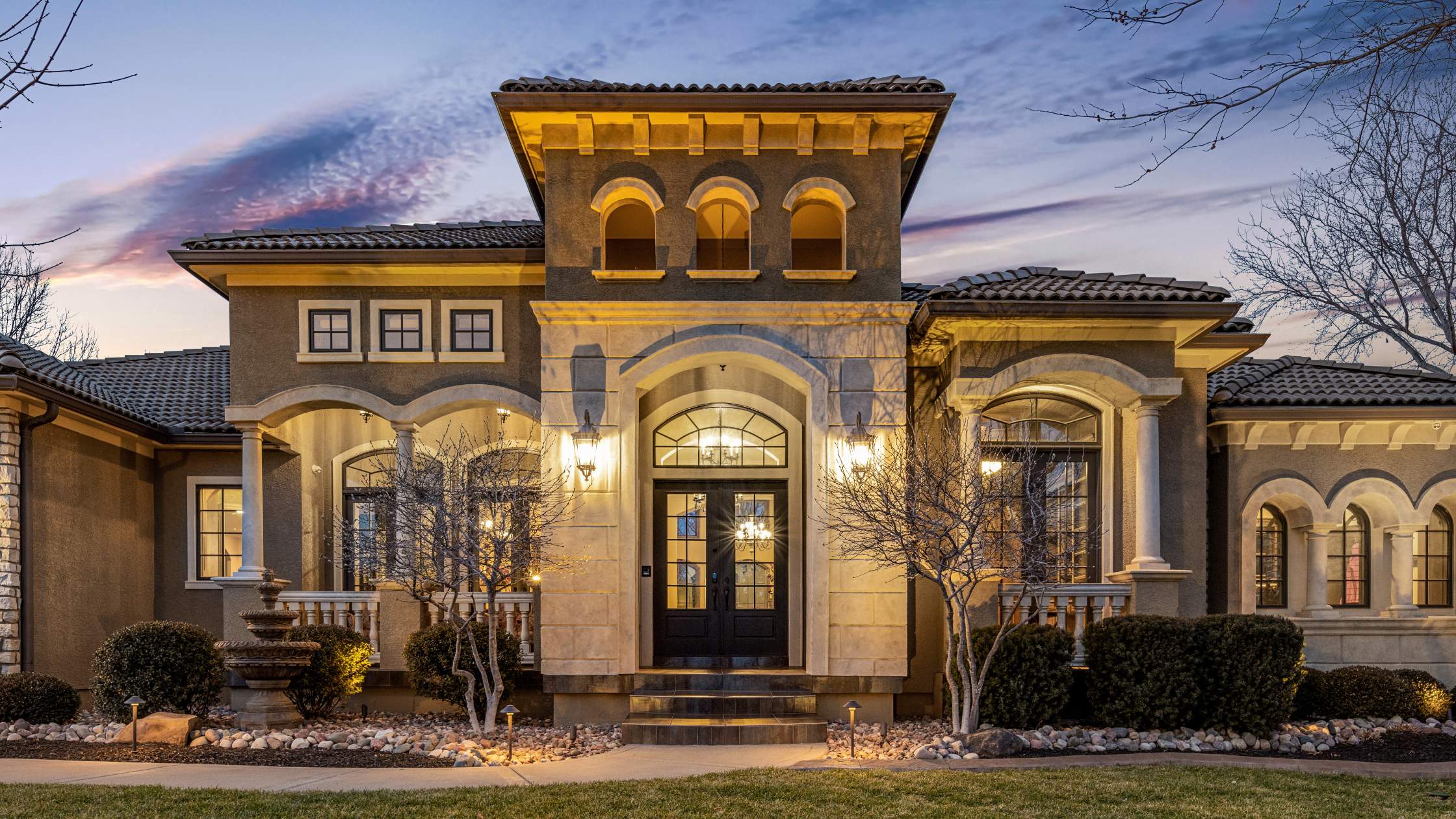 Twilight image of tuscan-style home with arched windows lit up at night.