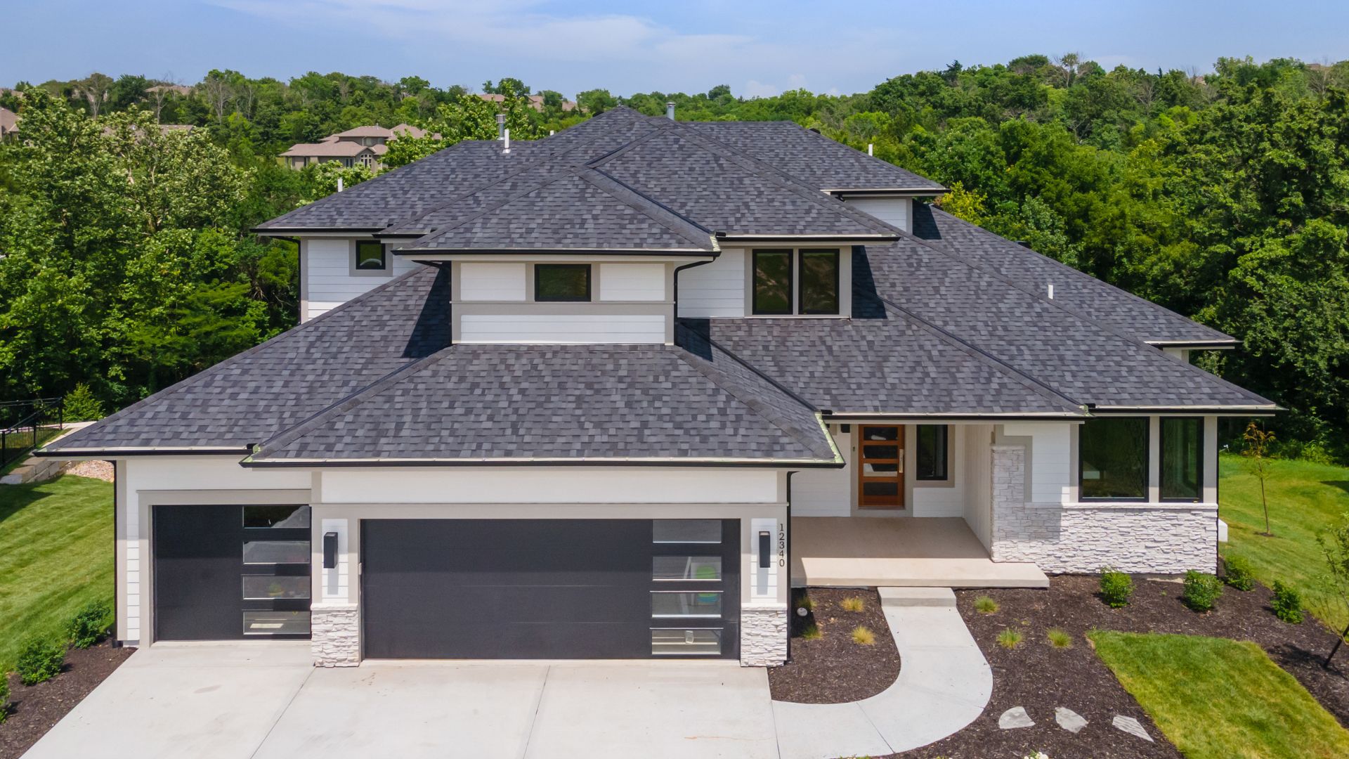 Front elevation shot of white contemporary home with black garage doors and dark roof.