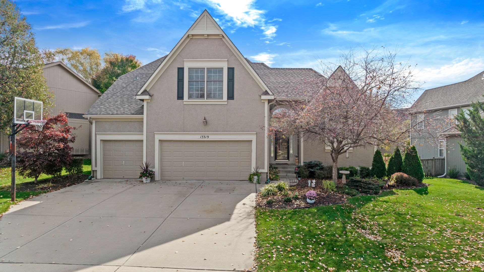 Front photo of a tan home with black shutters and a three car garage.