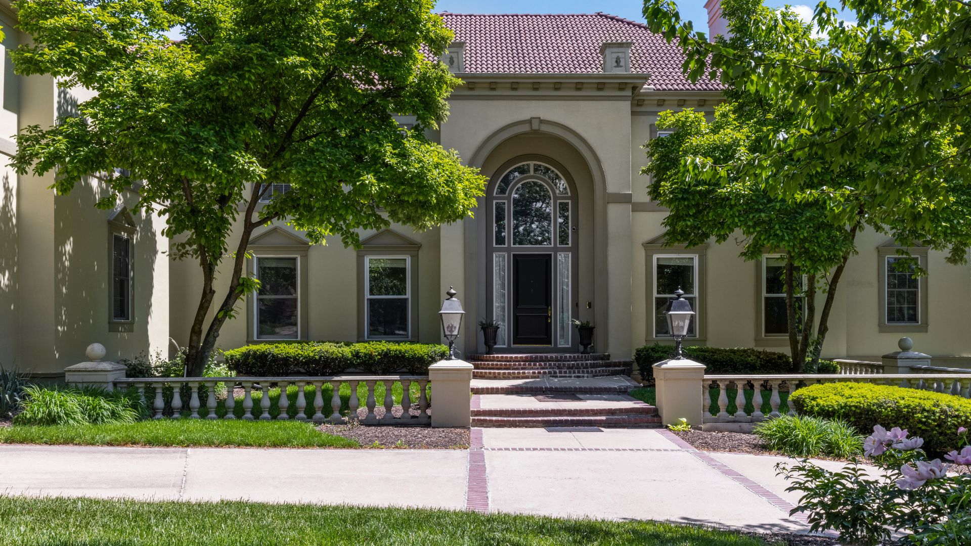 Front photo of home with green trees and arched entry way.