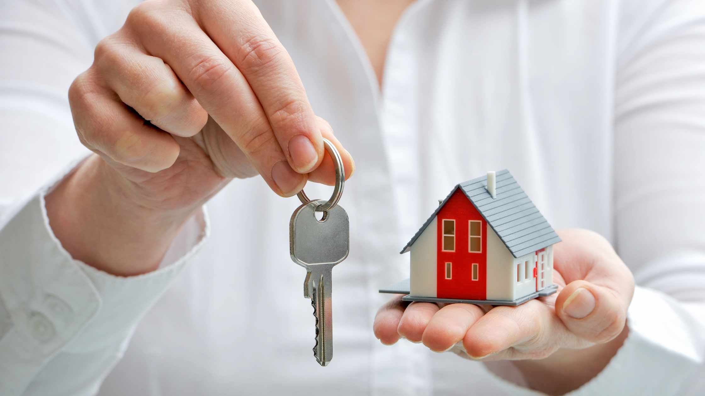 Hand with mini house and keys held out signifying home ownership.
