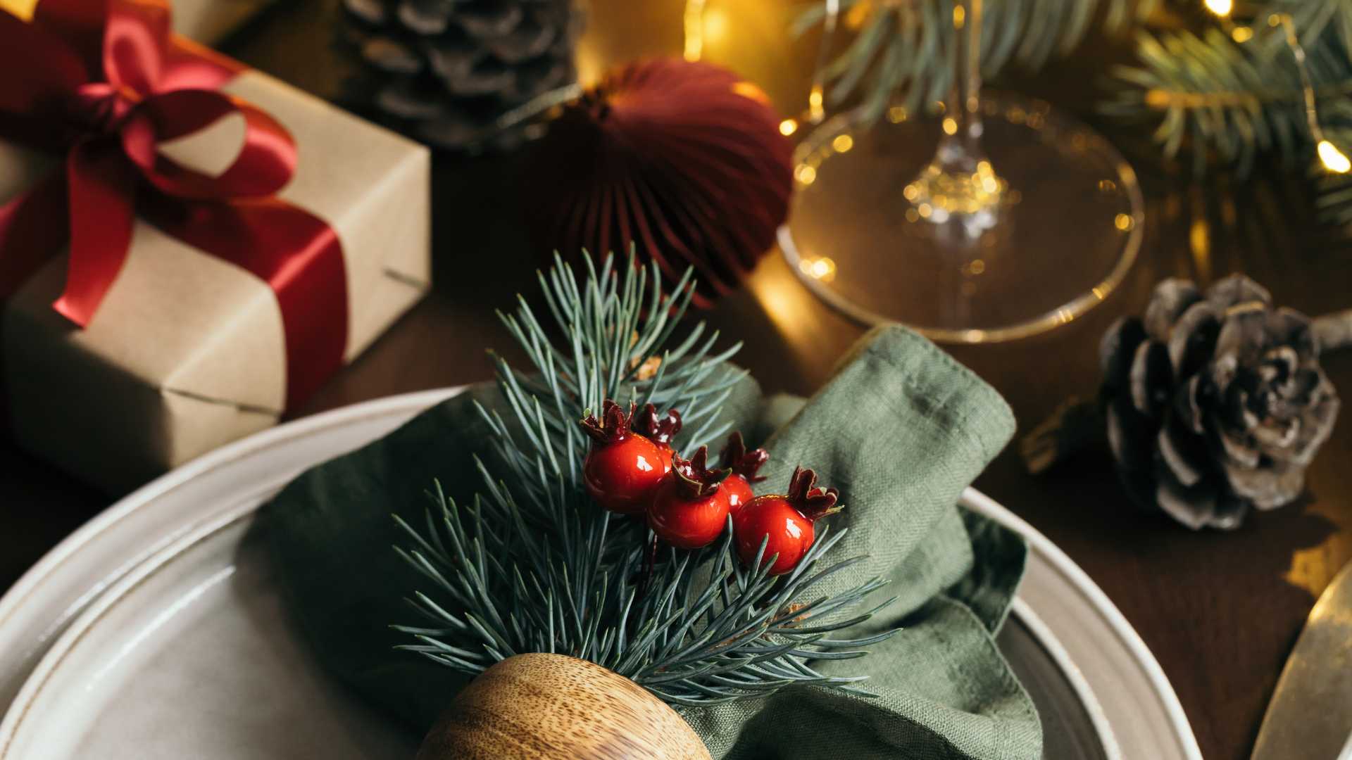 Photo of table setting set for Christmas with a wine glass, gift box & other decor.