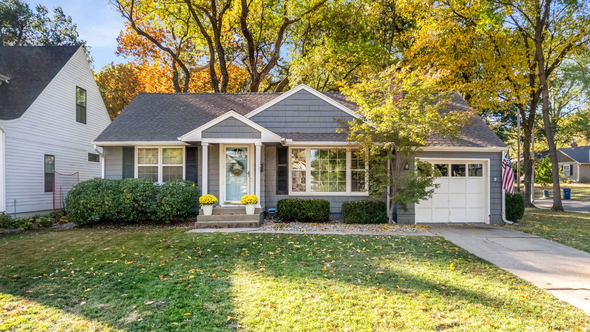Gray cape cod-style home with black shutters and a white garage door plus a teal front door.