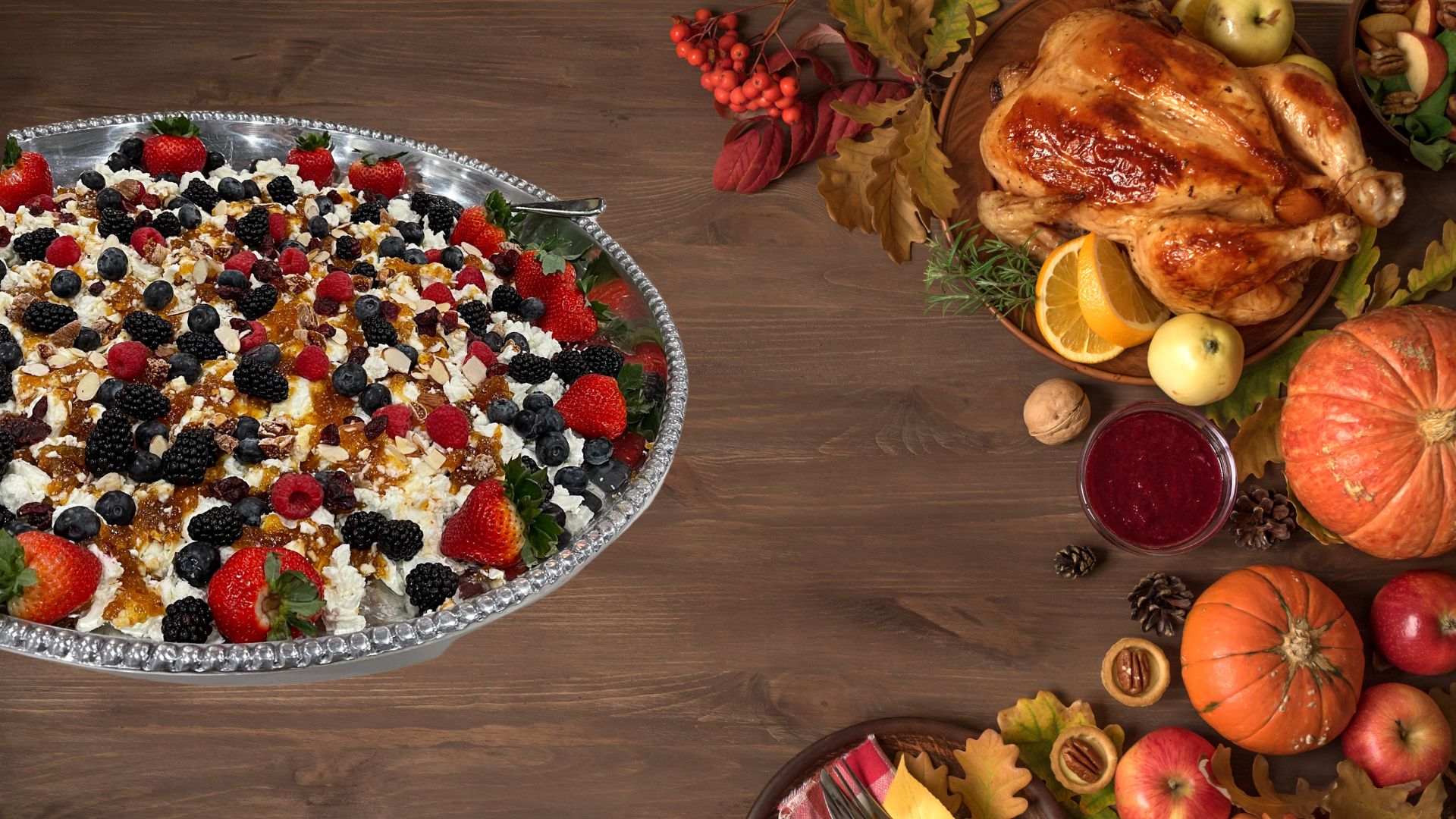 Table with food on it including a large platter with cheese and berries, turkey and pumpkins.