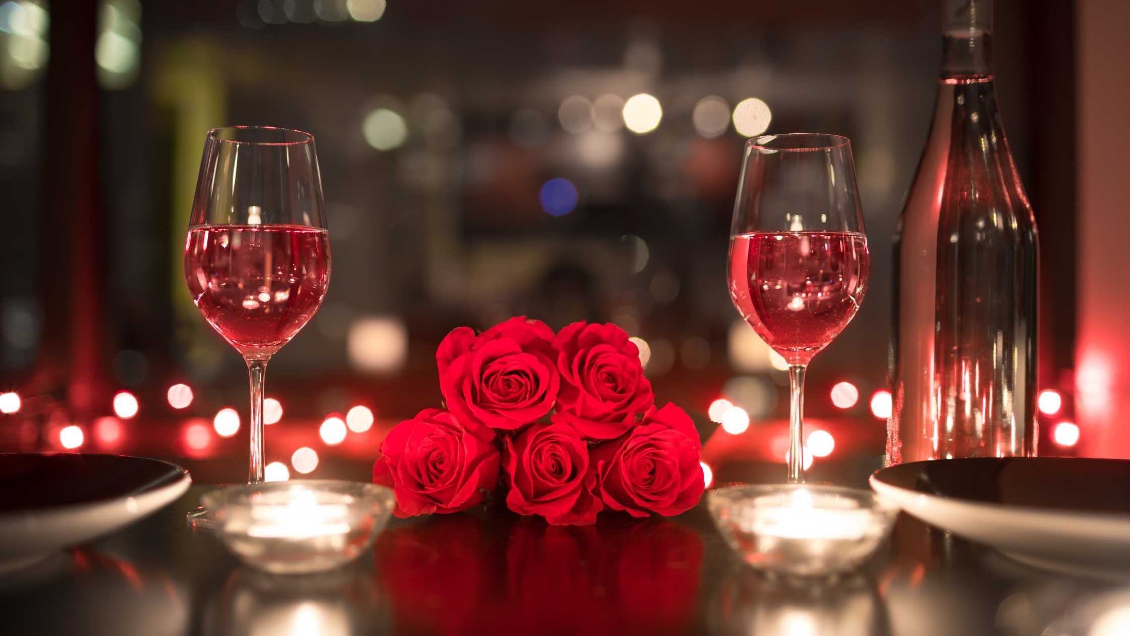 Two wine glasses filled with rose and flowers. candles and twinkling lights on the table that create a romantic look.